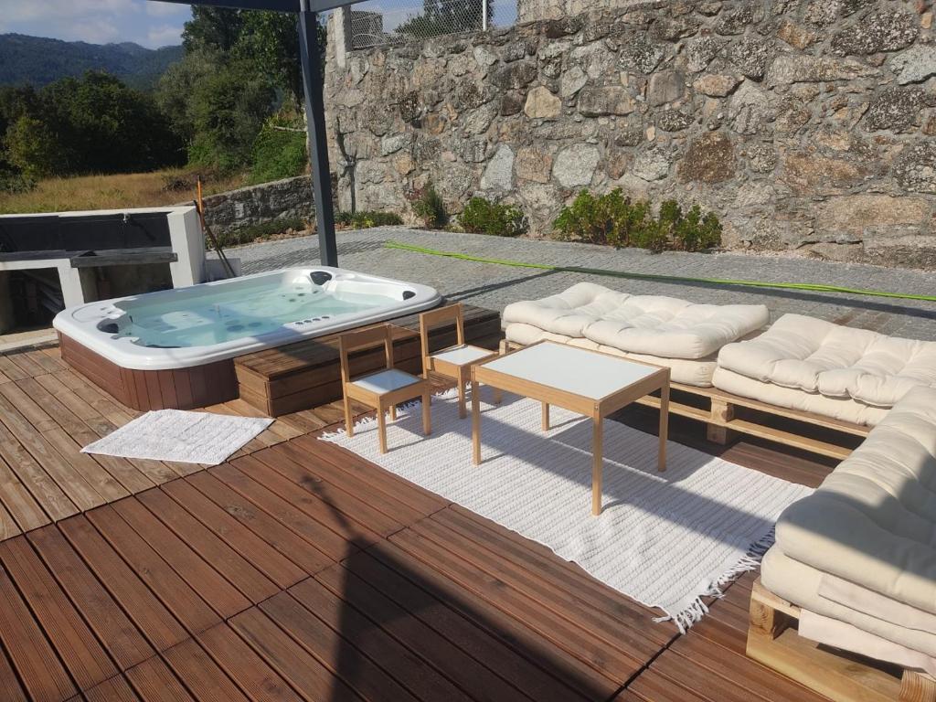 Jacuzzi no deck de madeira, com sofás de paletes e a churrasqueira encostada ao muro de pedra